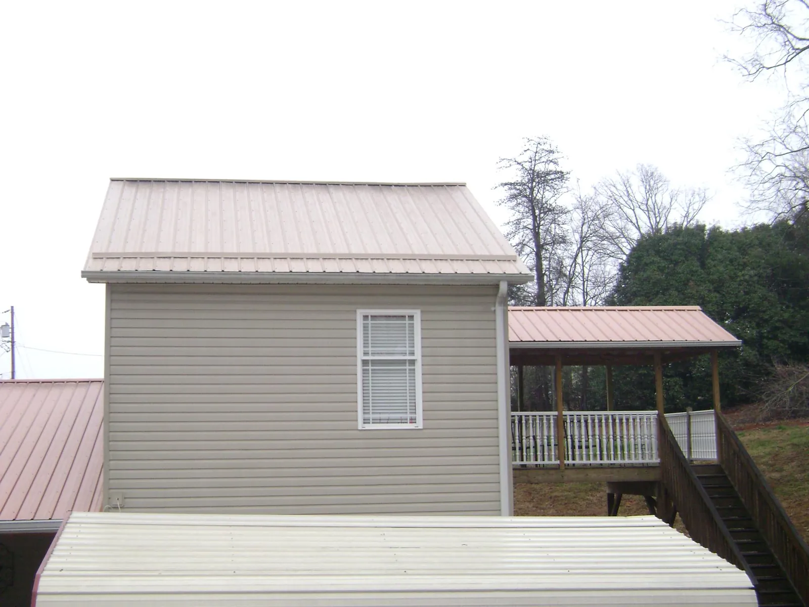 Tan metal roofs on a two story addition and attached porch, from a Roof Replacement job in Colbert